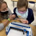 Ashlee Partin, B.A., COM/TVI, visually impaired and orientation instructor and mobility specialist, working with a student on a Brailler to increase to fine motor skills.
